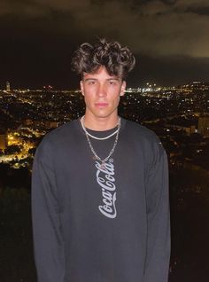 a young man with curly hair standing in front of a cityscape at night