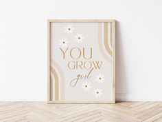 a framed poster with the words you grow and daisies in gold foil on a white wall