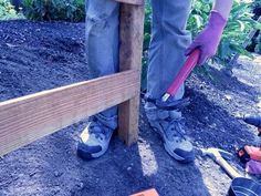 a person wearing purple gloves and holding a red tool near a wooden fence in the dirt