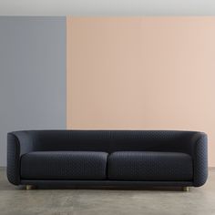 a black couch sitting in front of a pink and gray wall with a wooden frame