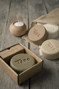 two soaps in a cardboard box on a wooden table next to a tea light