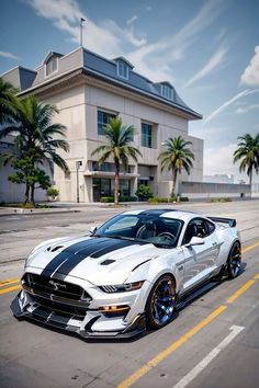 a white and black mustang parked in front of a large building with palm trees around it