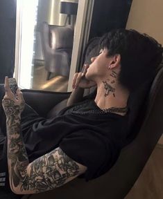 a man with tattoos on his arm laying in a black chair and looking at the camera