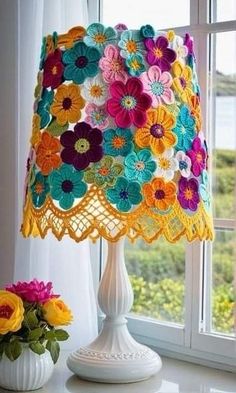 a crocheted lamp shade sitting on top of a table next to a window