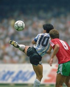 two men playing soccer on a field with spectators in the stands watching from behind them