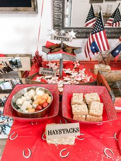 a red table topped with trays of food next to american flags and other decorations