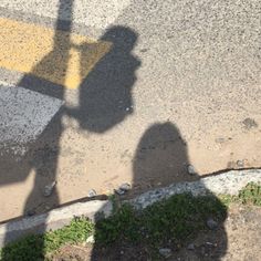 the shadow of a person holding an umbrella over their head is cast on the pavement