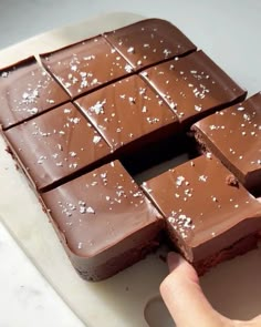 a person holding a piece of chocolate in front of some pieces of cake on a cutting board