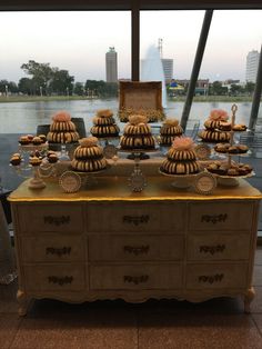 an old dresser with desserts on it in front of a window overlooking the water