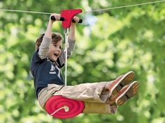 a young boy riding on top of a zip line in the air while holding onto a red handle