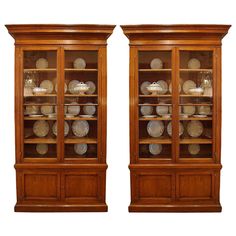 two wooden shelves with glass doors and plates on them in front of each other, side by side