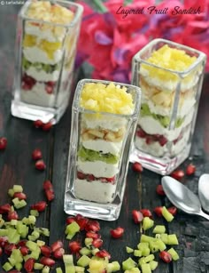 three desserts with fruit in them sitting on a table next to spoons and flowers