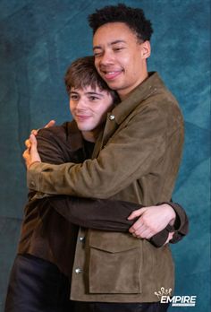 two young men hugging each other in front of a blue background