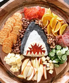 a wooden platter filled with different types of cheeses, crackers and fruit