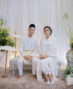 a man and woman sitting on a bench in front of a white curtained wall