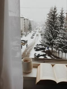 an open book sitting on top of a window sill in front of a snowy street