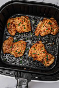 four pieces of chicken cooking in an air fryer with parsley on the side