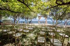 an outdoor ceremony set up with white linens and gold chairs, overlooking the water