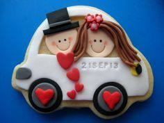 a decorated cookie with two people in a car and hearts on the side, sitting on a blue surface