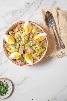 a bowl filled with meat and boiled eggs on top of a table next to a spoon