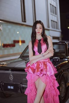 a woman in a pink dress standing next to a black car