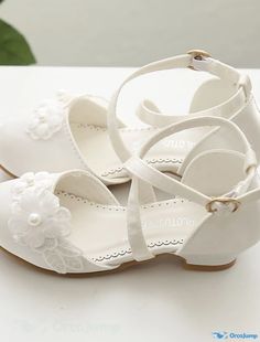 a pair of white baby shoes with flowers on the front and bottom, sitting on a table