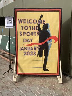 a welcome to the sports day sign in front of a wall with an image of a man holding a red ribbon