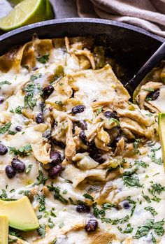 a skillet filled with chicken, black beans and tortilla shells topped with avocado wedges