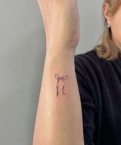 a woman's arm with a small bow tattoo on the left side of her wrist