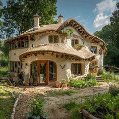 a small house with a thatched roof in the middle of a garden and surrounded by greenery