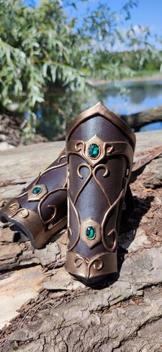 two brown leather cuffs with green jewels on them sitting on a tree branch next to water