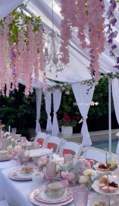 a table set up for a tea party with pink flowers hanging from the ceiling and white draping