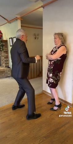 an older man and woman are dancing in front of a fireplace with christmas decorations on the mantle