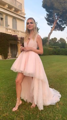 a woman in a pink dress posing for a photo on the grass near a house