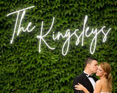 a bride and groom standing in front of a green wall with the words the kingsleys on it