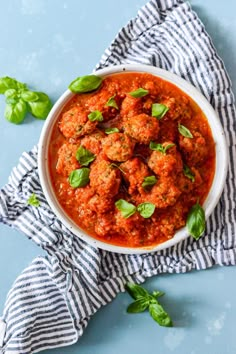 a white bowl filled with meatballs covered in marinara sauce and fresh basil leaves