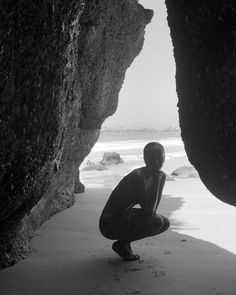 a man kneeling down in front of two large rocks on the beach next to the ocean