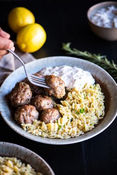 someone is holding a fork over some pasta with meatballs and sauce on the side