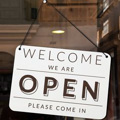 a white sign hanging from the side of a glass door that says, welcome we are open please come in