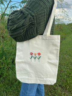 a person is holding a white bag with flowers painted on it in front of some grass