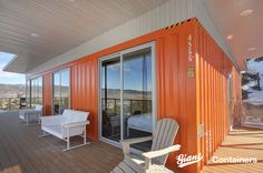 an orange shipping container is sitting on a deck with white chairs and a table in front of it