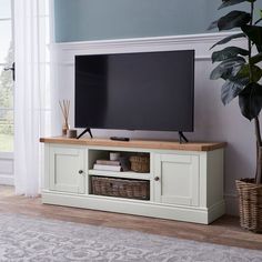 a flat screen tv sitting on top of a wooden entertainment center next to a potted plant