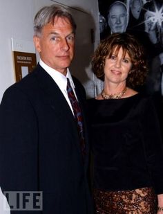 a man and woman standing next to each other in front of a wall with pictures on it