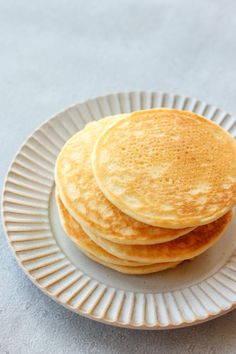 three pancakes on a white plate sitting on top of a gray tablecloth covered floor