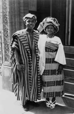 two people standing next to each other in front of a building wearing hats and scarves