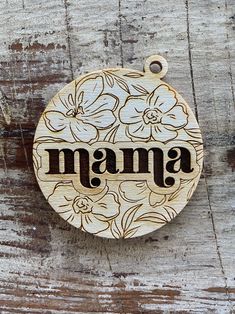 a wooden sign that says mama on it with flowers and leaves around the word in black ink