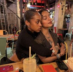 two women sitting at a table with drinks in front of them and one holding the other