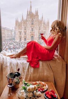 a woman in a red dress sitting on a window sill with food and drink