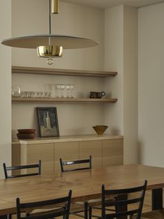 a dining room table with black chairs and wooden shelves on the wall behind it,