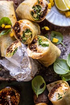 several burritos are wrapped in foil and garnished with fresh herbs, on a table